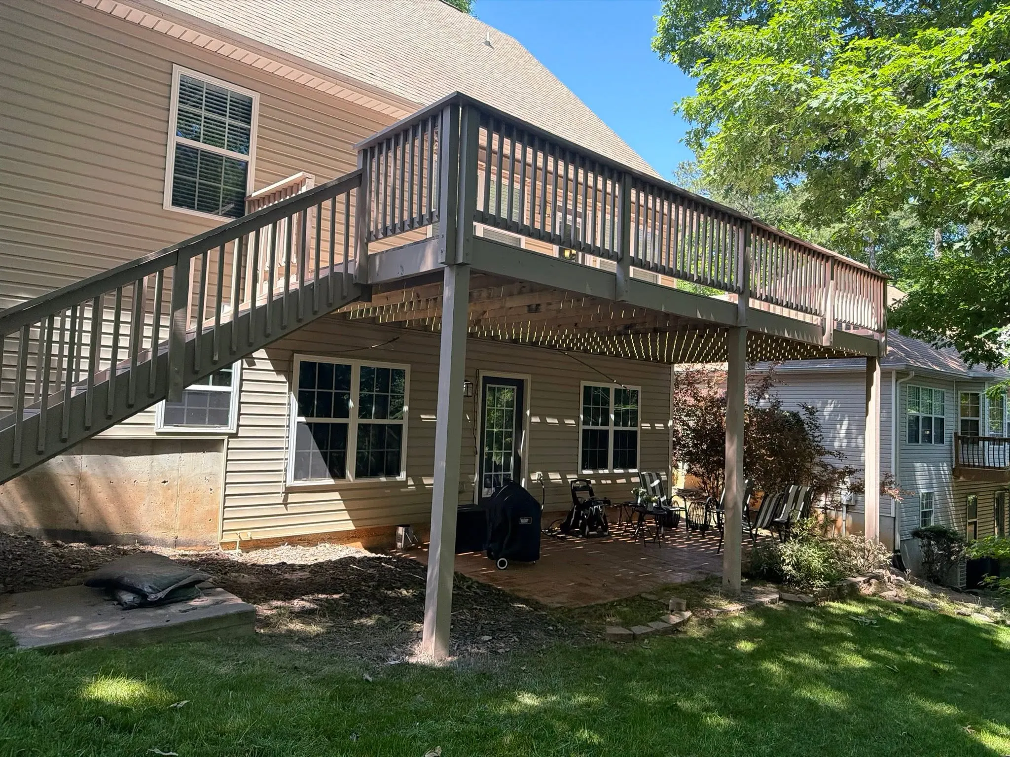 Large elevated deck with a long staircase down to a covered patio at a two-story Villa Rica home, full summer green