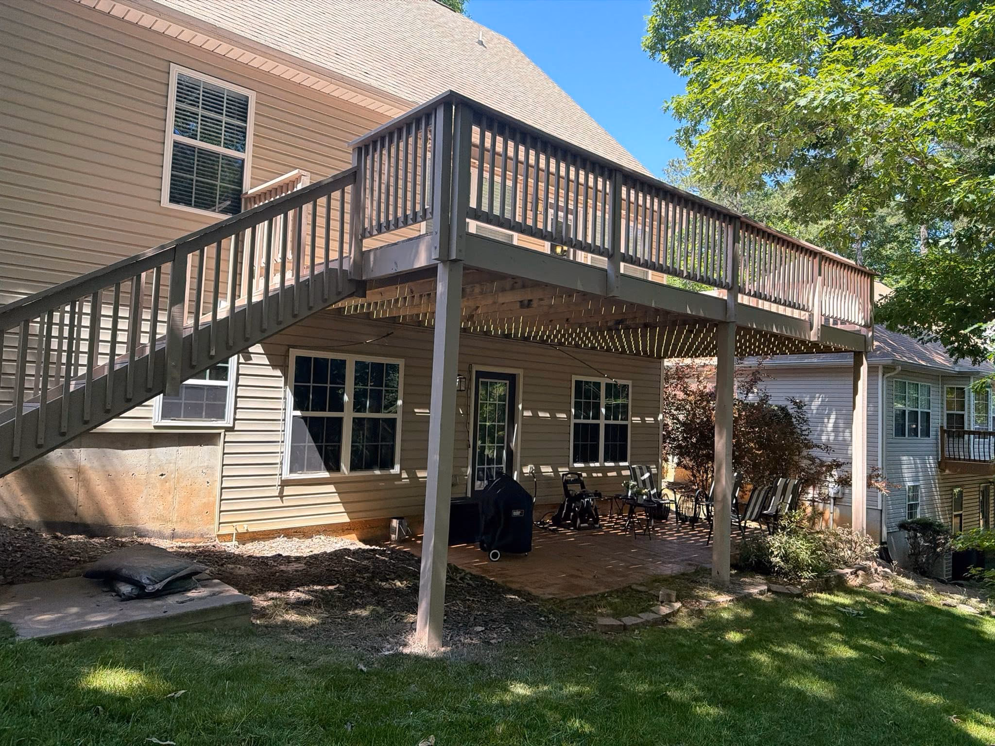 Large elevated deck with a long staircase down to a covered patio at a two-story Villa Rica home, full summer green