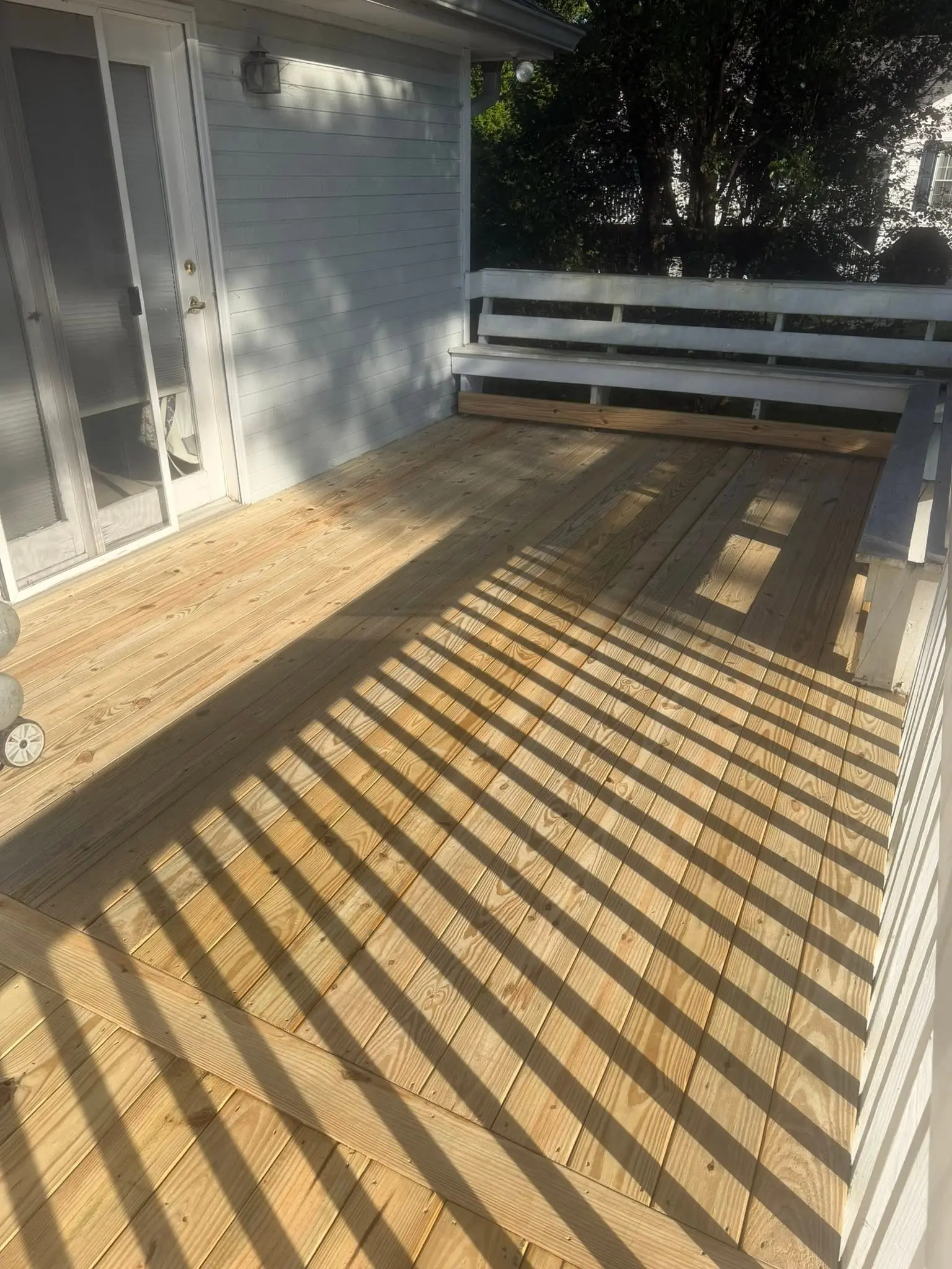 Deck floor with new pressure-treated boards beside a pair of glass doors