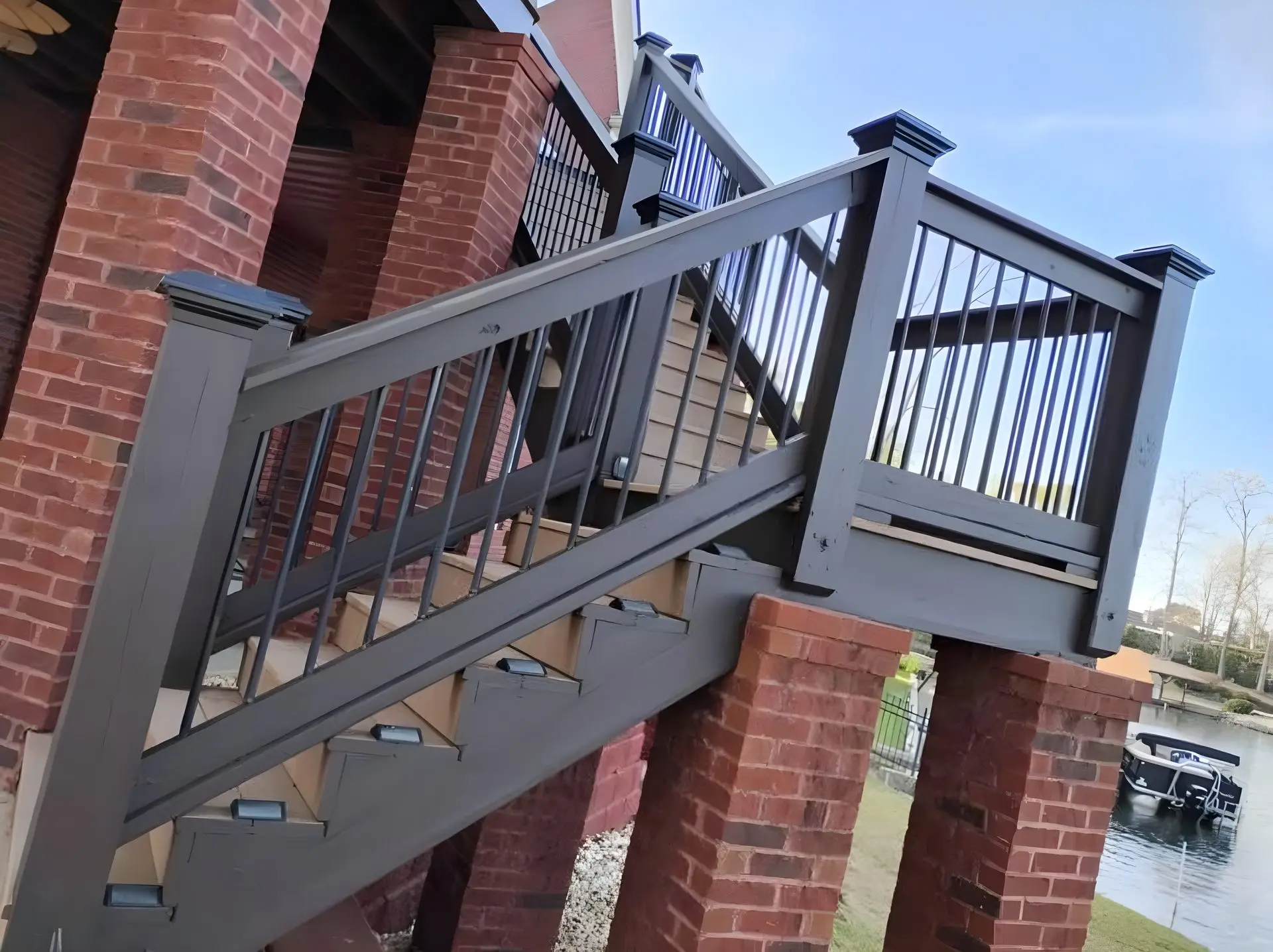 Deck stairs with a black guard and handrail between brick columns, a pontoon boat at a dock below