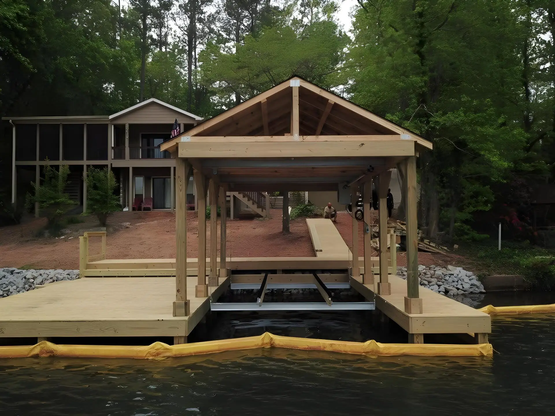 Boat lift cradle under a newly built gable-roof boathouse, silt barrier in the water
