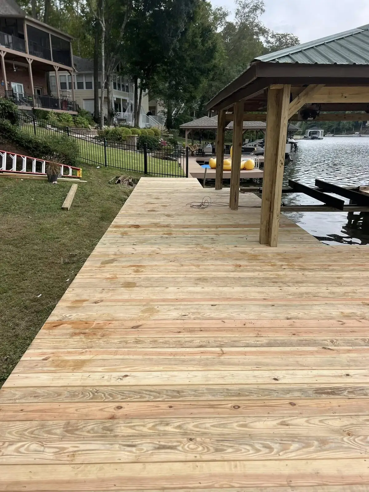 New pressure-treated dock walkway leading to a covered boathouse with a green metal roof