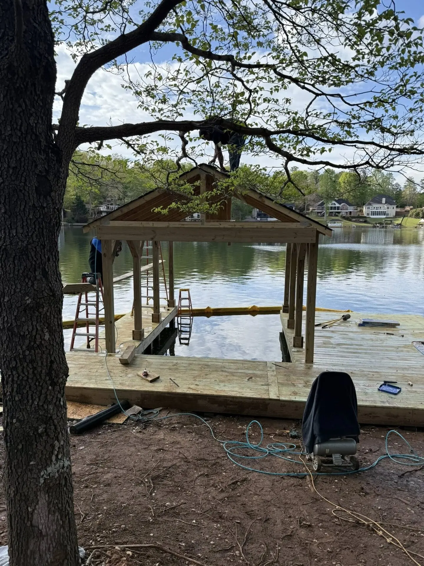 Crew member framing a boathouse roof over the lake, homes on the far shore