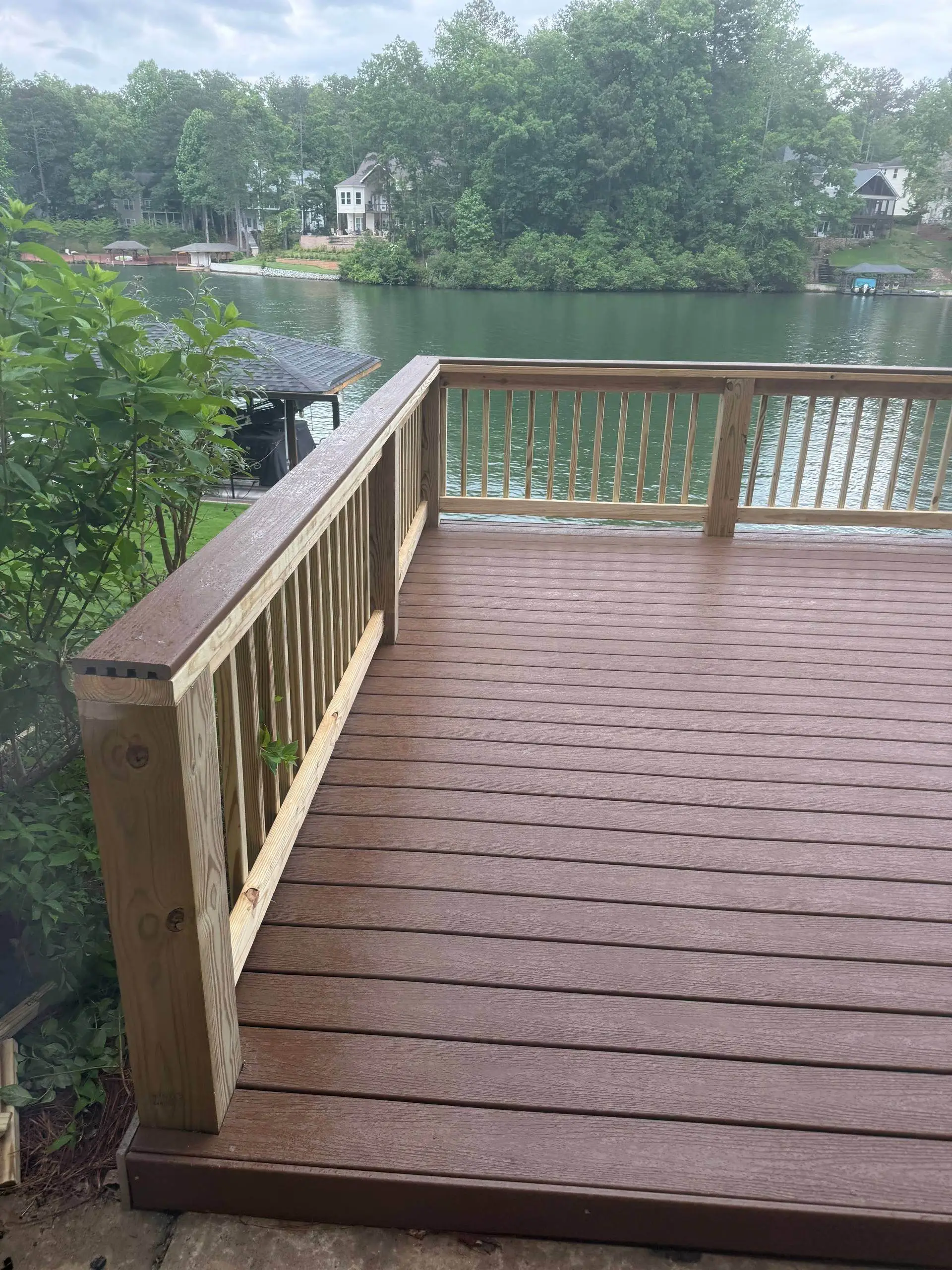 Finished composite deck with a wood rail, view out to a private boathouse dock across the water.