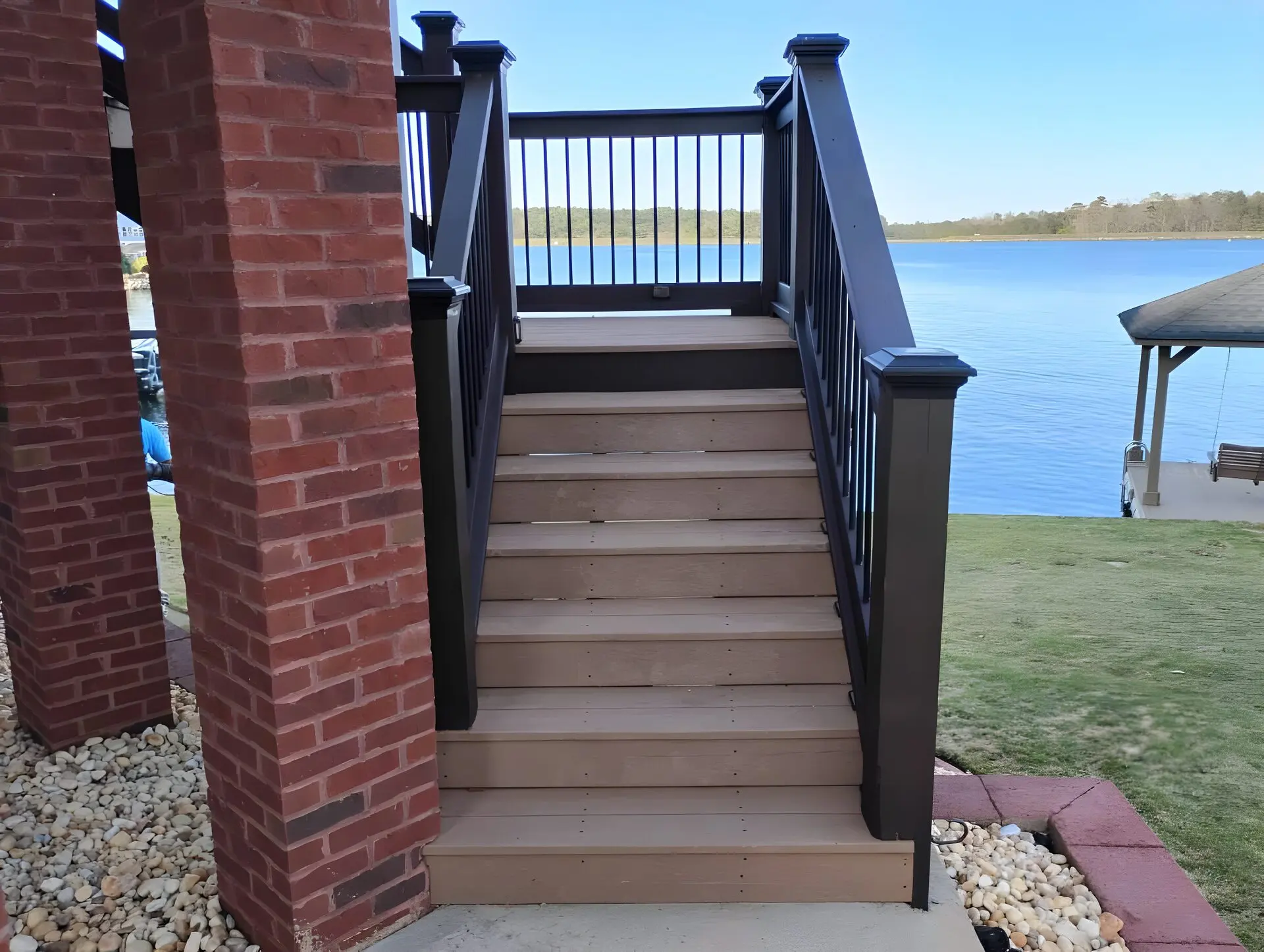 Deck stairs with dark-stained rails and posts between brick columns, lake behind