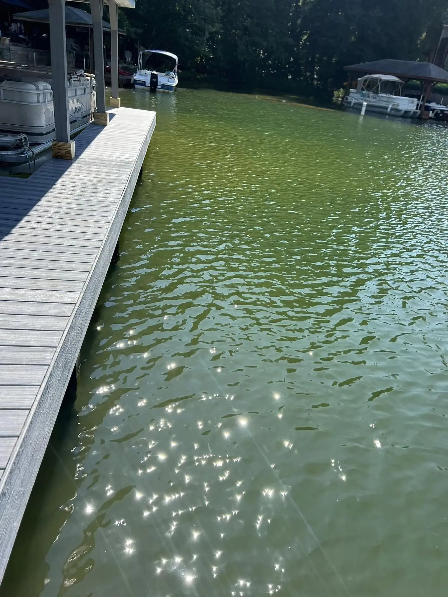 A gray composite dock walkway with covered boat slips and pontoon boats on a west Georgia lake