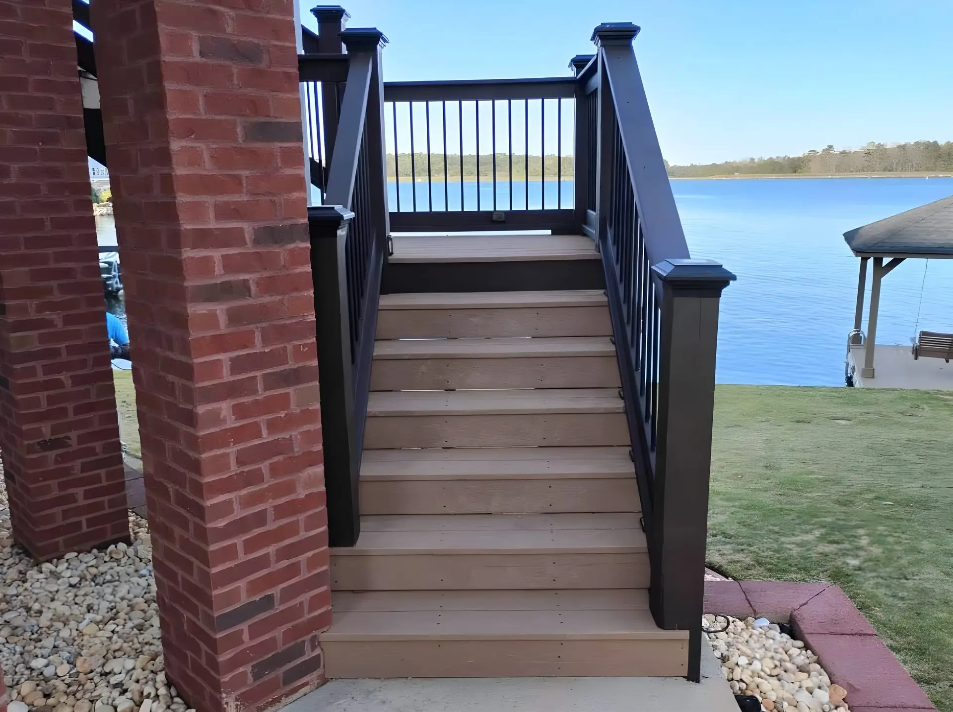 Composite deck stairs with black rail descending between two brick columns