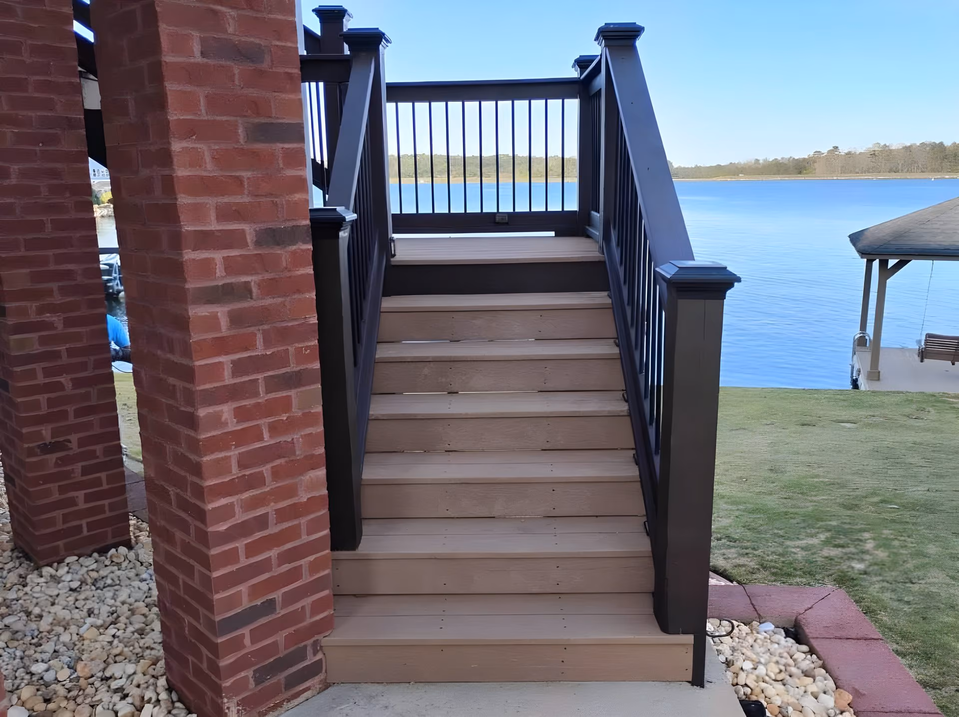 Composite deck stairs with black rail descending between two brick columns