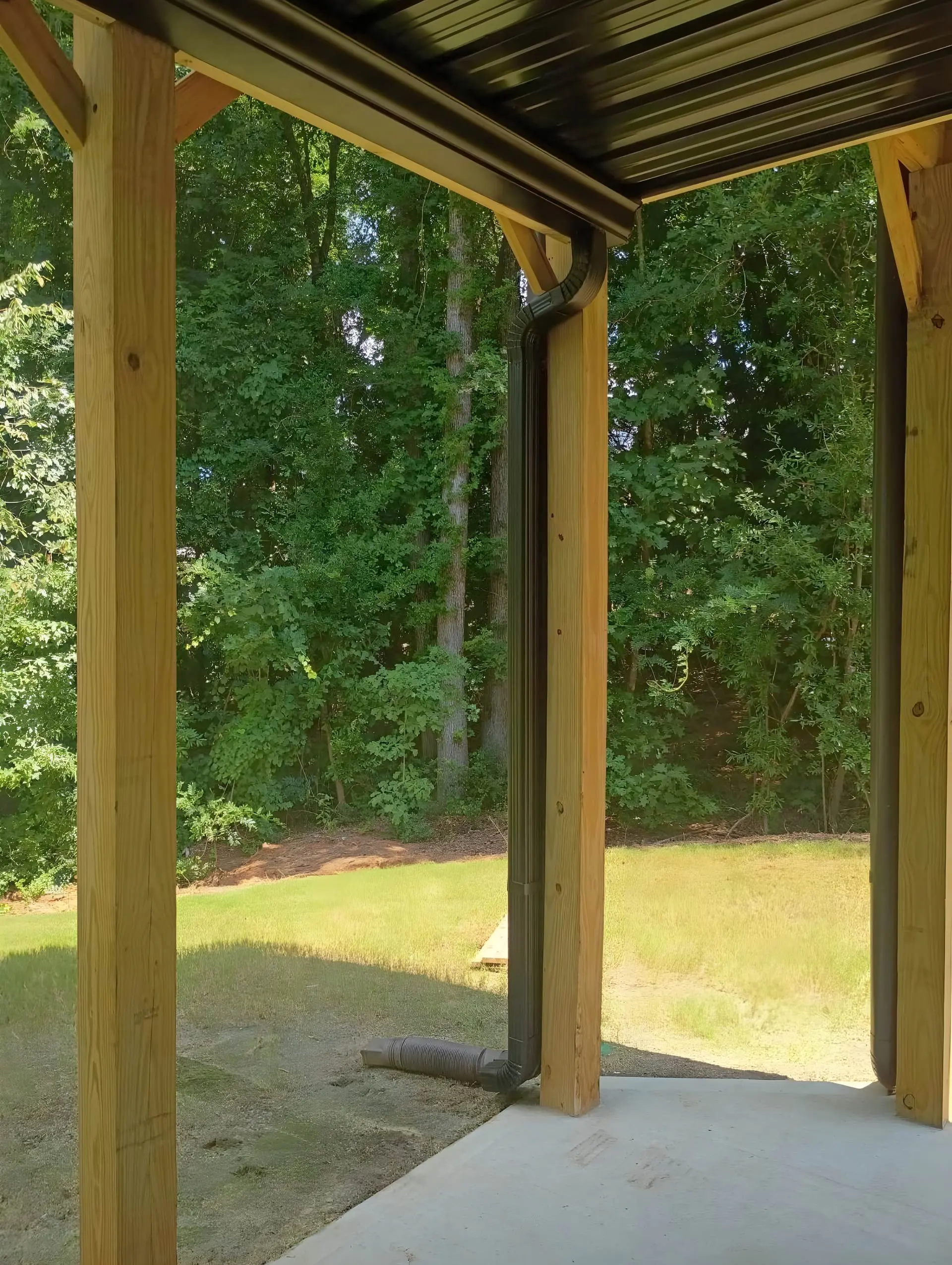 New covered patio with a metal roof, wood posts, and a clean poured concrete slab facing a green lawn