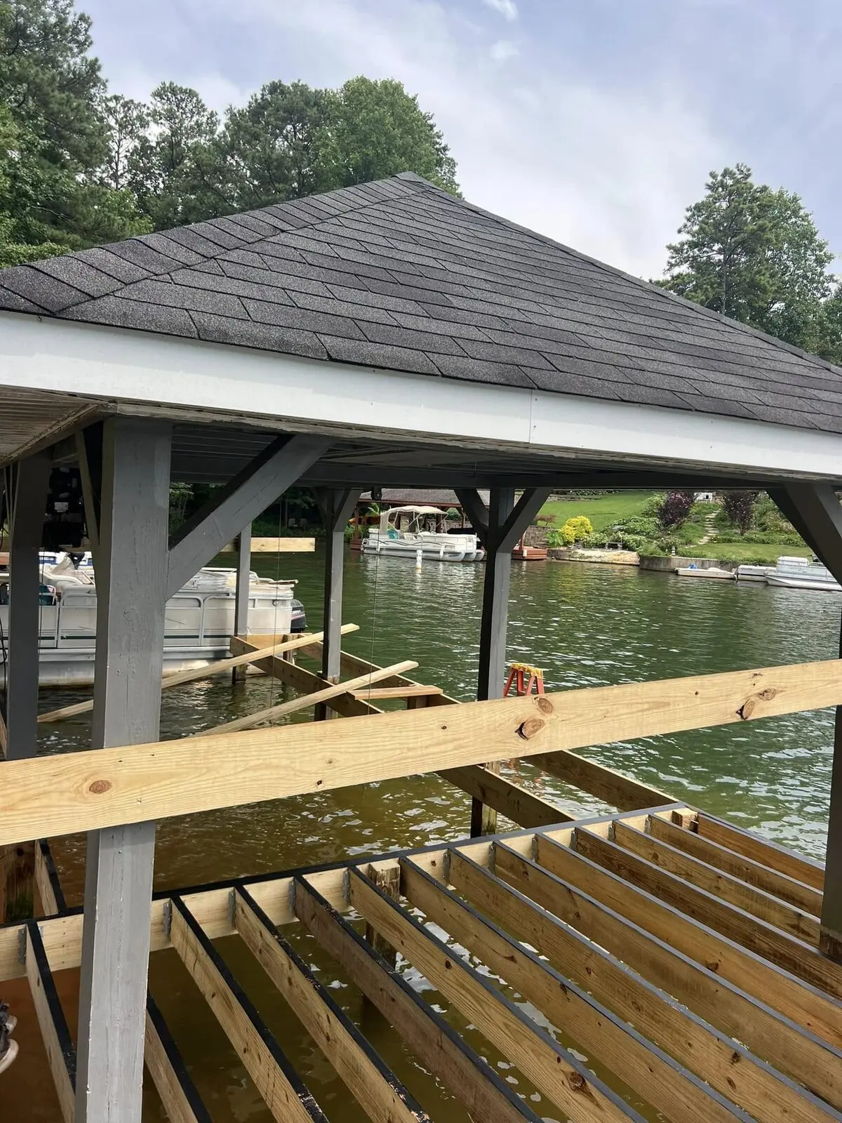 New dock joists with hangers set under a covered slip, pontoon boats behind