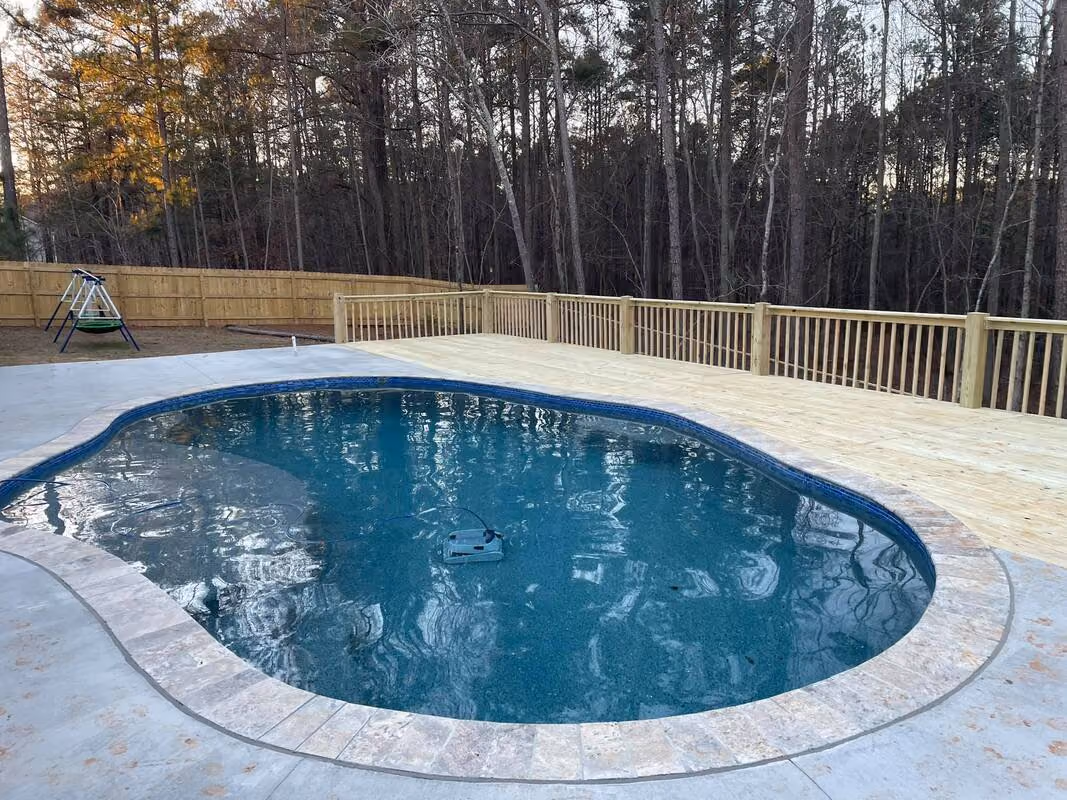 New wood deck and privacy fence running along the back of an in-ground pool at dusk