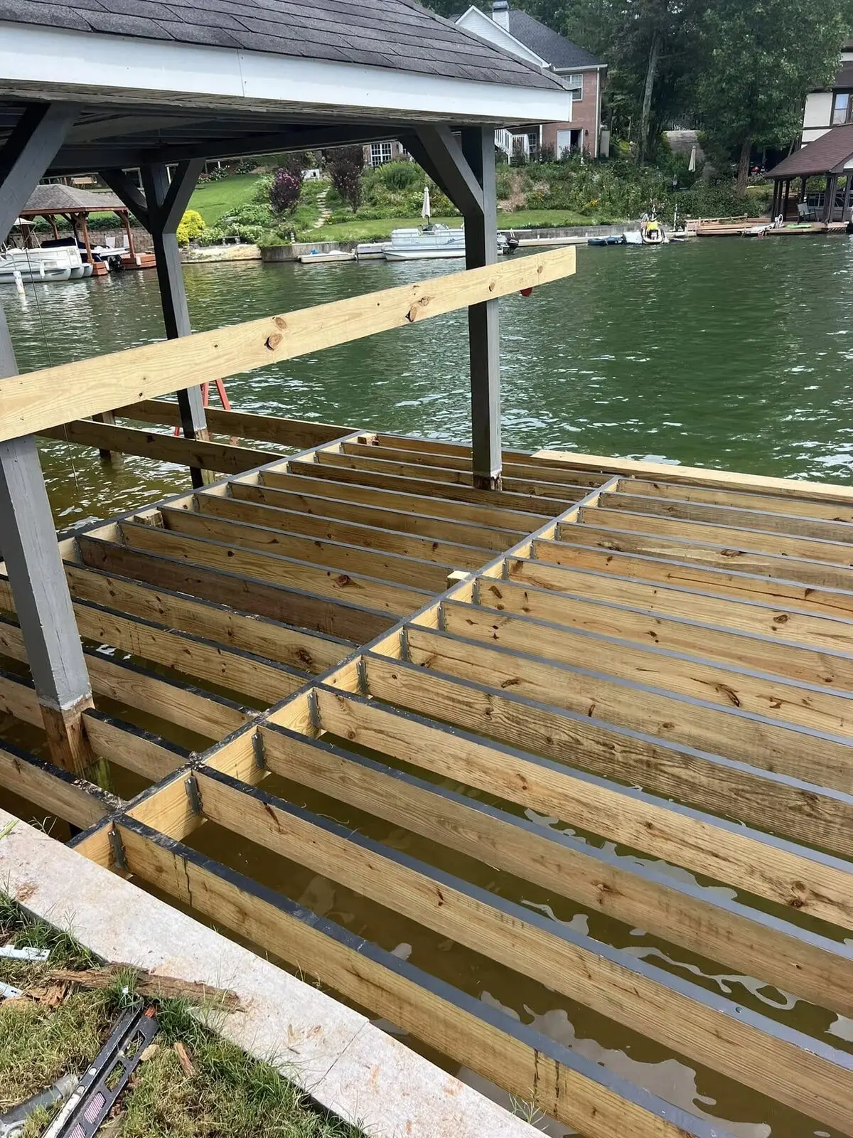 New dock frame of bare joists stretching toward open water, lake homes visible across the cove