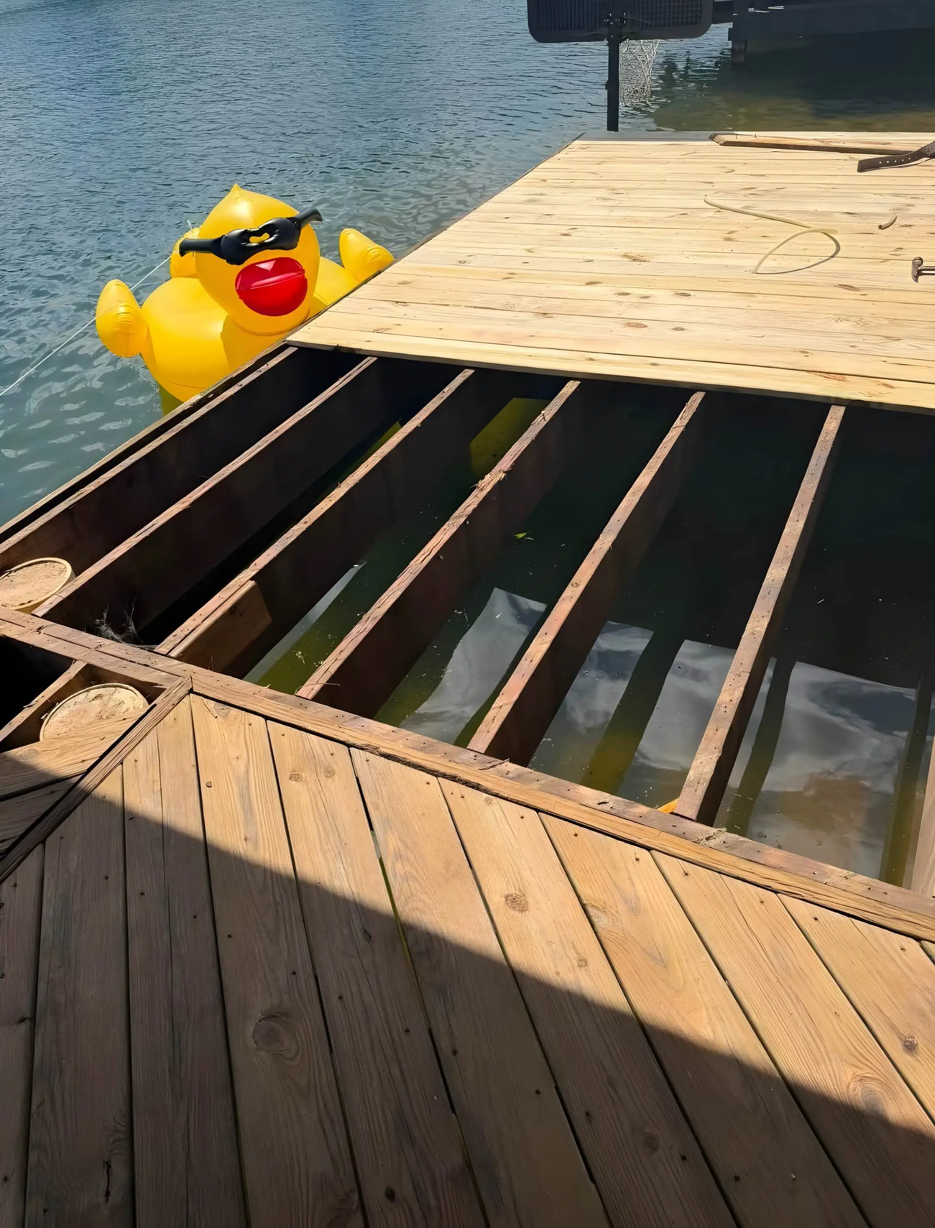 Dock decking installation with one section still open joists over the water, no decking boards on that section yet, an inflatable rubber duck floating alongside.