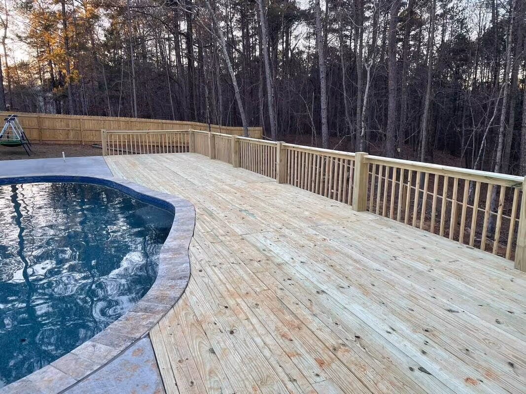 Wide pressure-treated pool deck curving around an in-ground pool at sunset