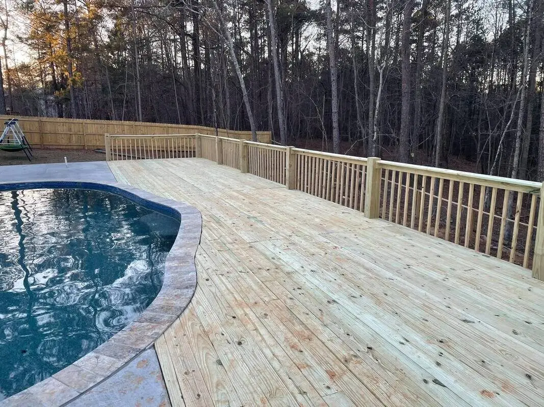 Wide sweeping pressure-treated pool deck curving around an in-ground pool at sunset