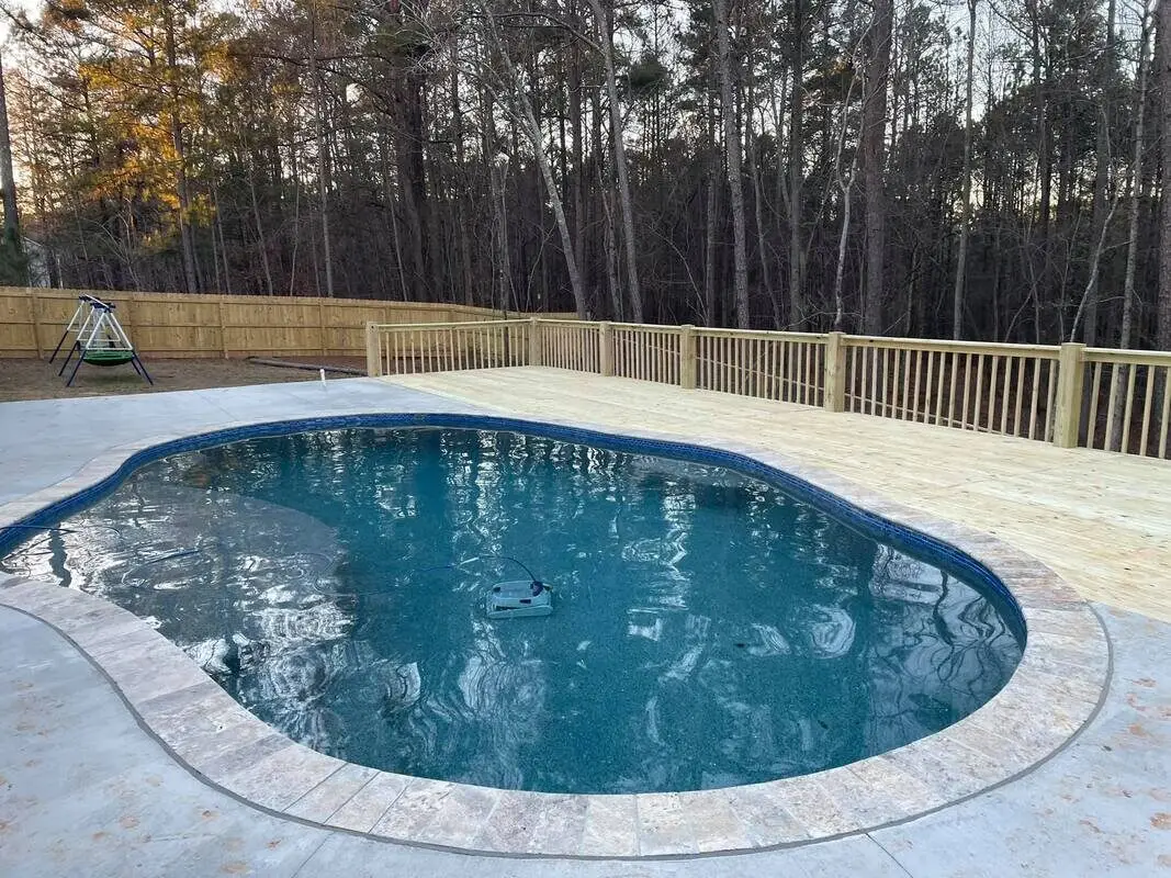 New pressure-treated pool deck perimeter with a fenced yard and swing set, dusk light