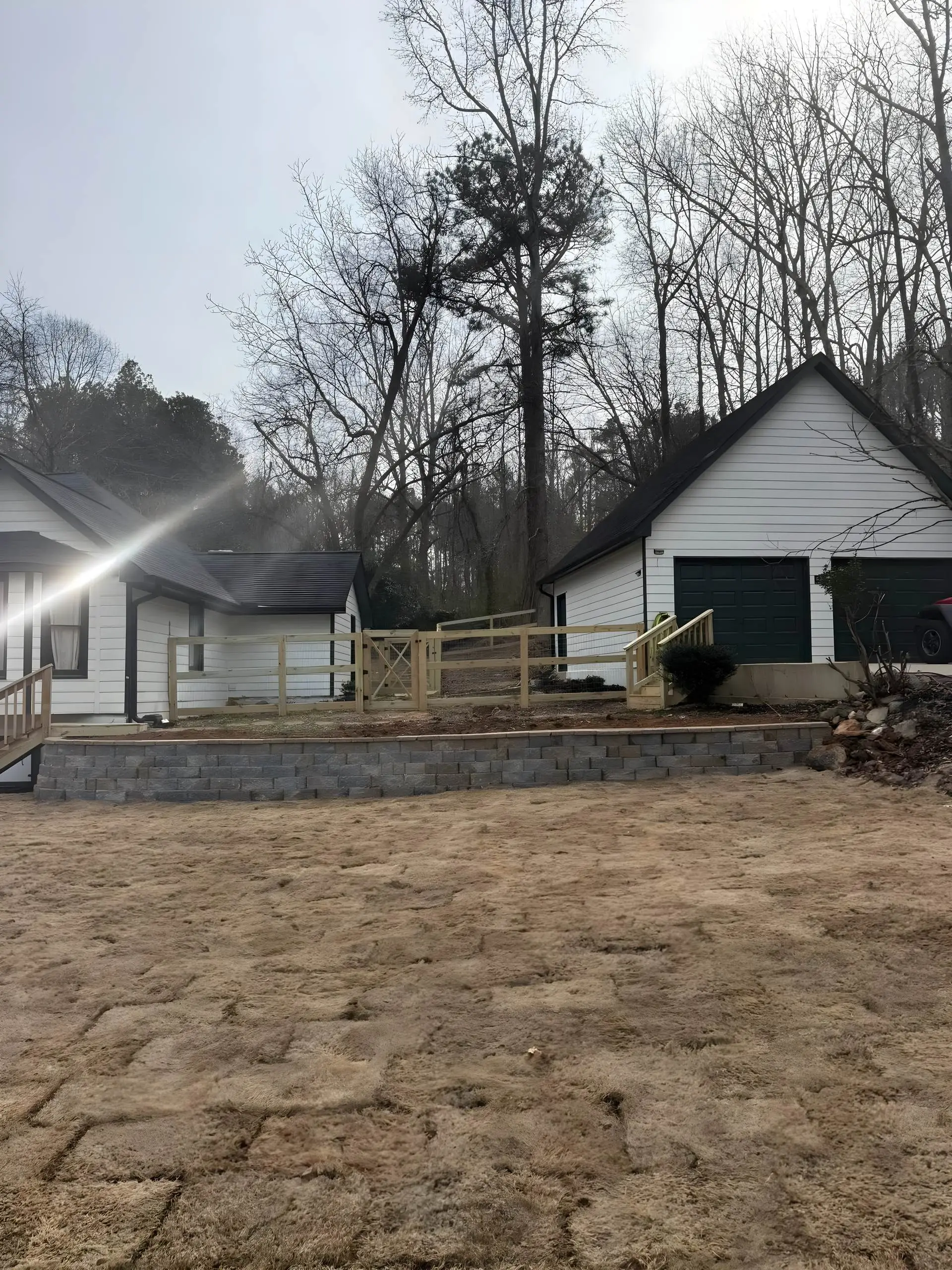 Yard transformation with a block retaining wall, new farm fence and gate, and fresh sod at a white farmhouse.