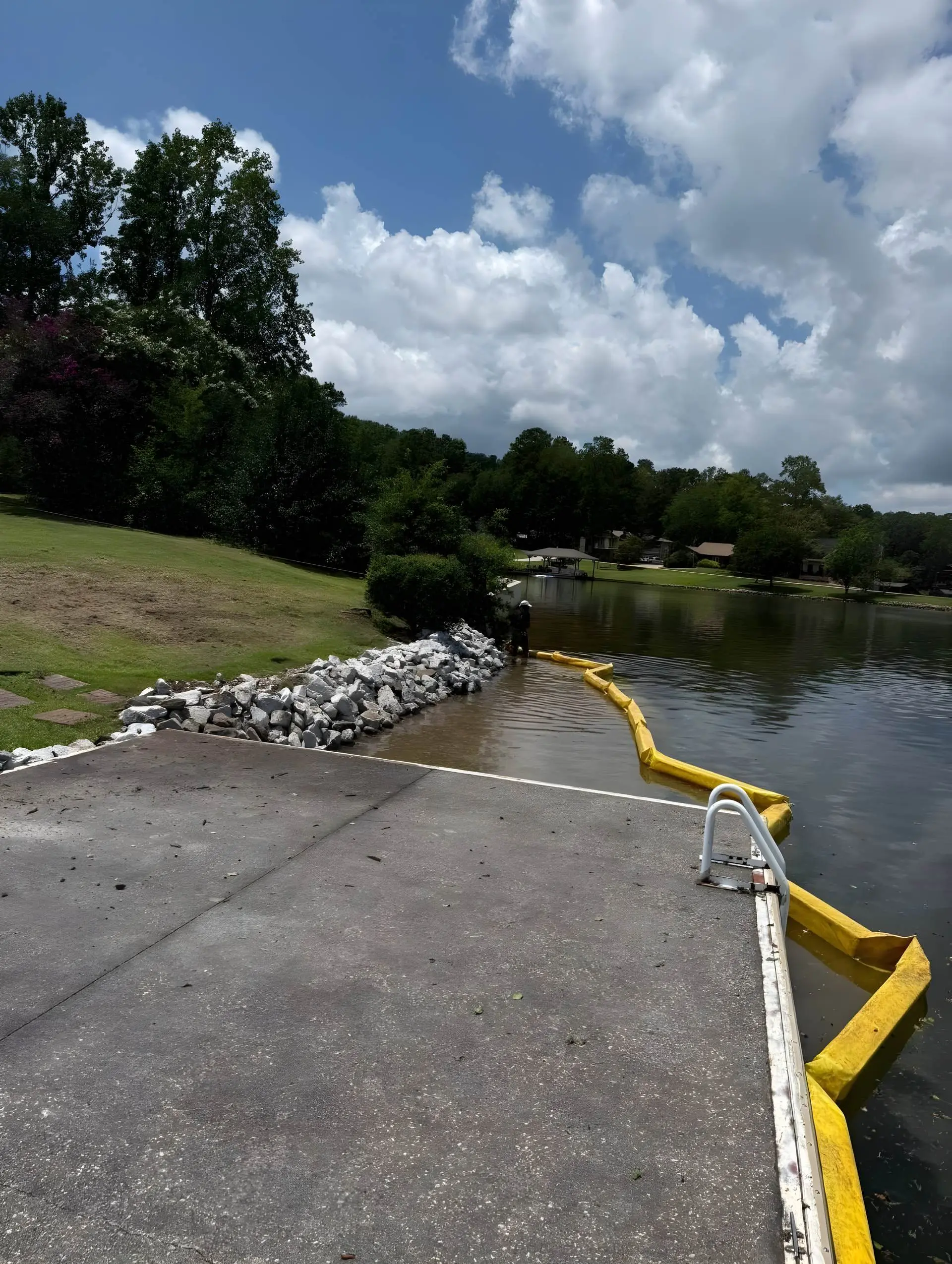 Riprap bank repair beside a concrete pad with a yellow silt curtain floating in the water