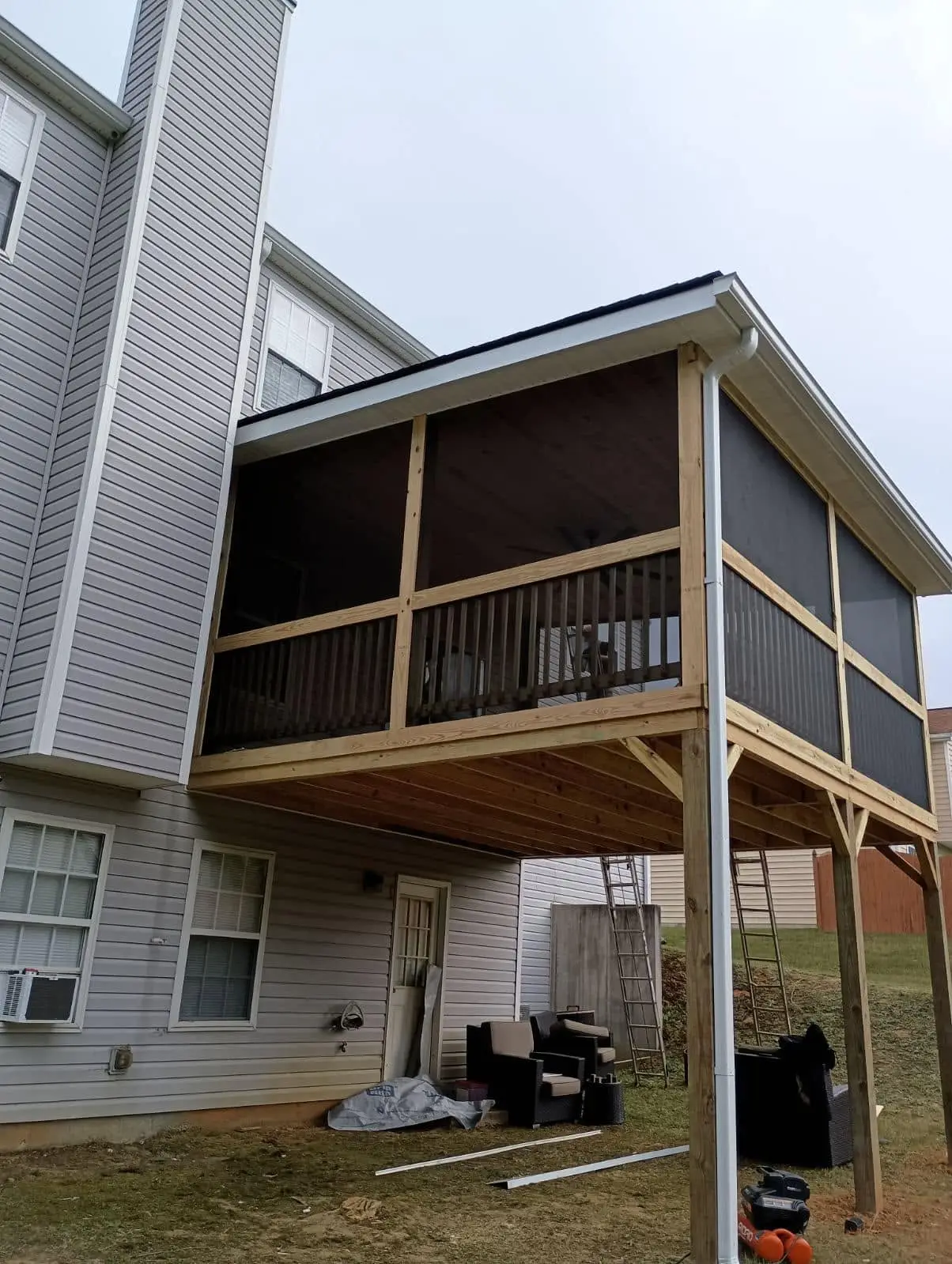 Two-story vinyl-sided house with a new screened deck on treated posts and braces under a pitched roof