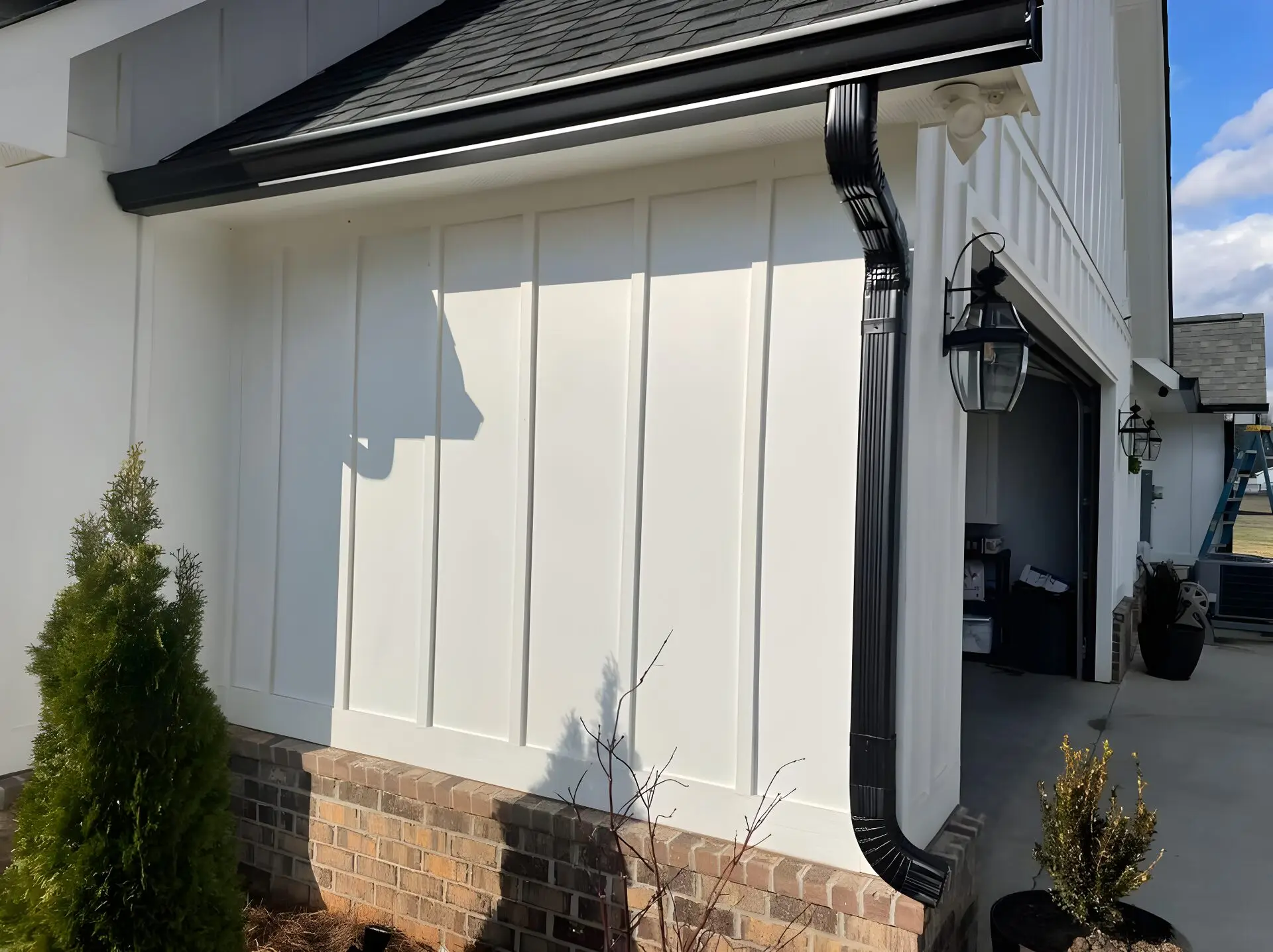 Black seamless gutter along a roofline and a black downspout on a white board-and-batten farmhouse wall