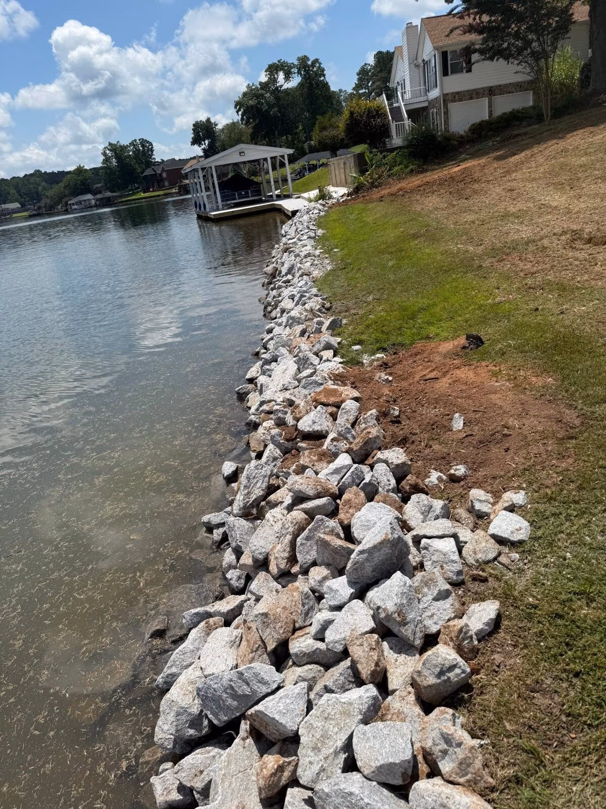 Finished rip-rap stone seawall along a Fairfield Plantation lake bank, with a covered dock across the water