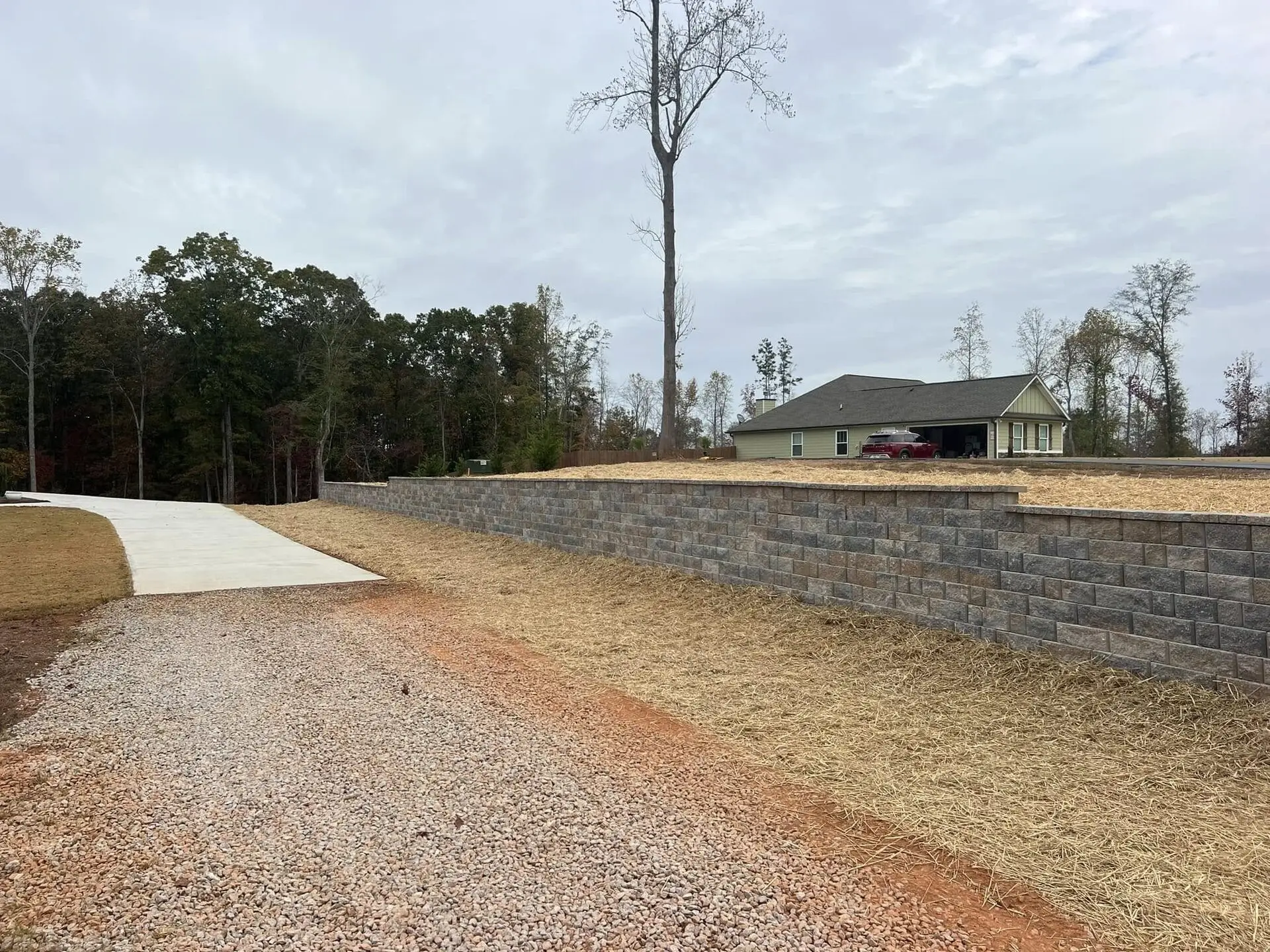 Long segmental-block retaining wall with freshly graded and strawed yard