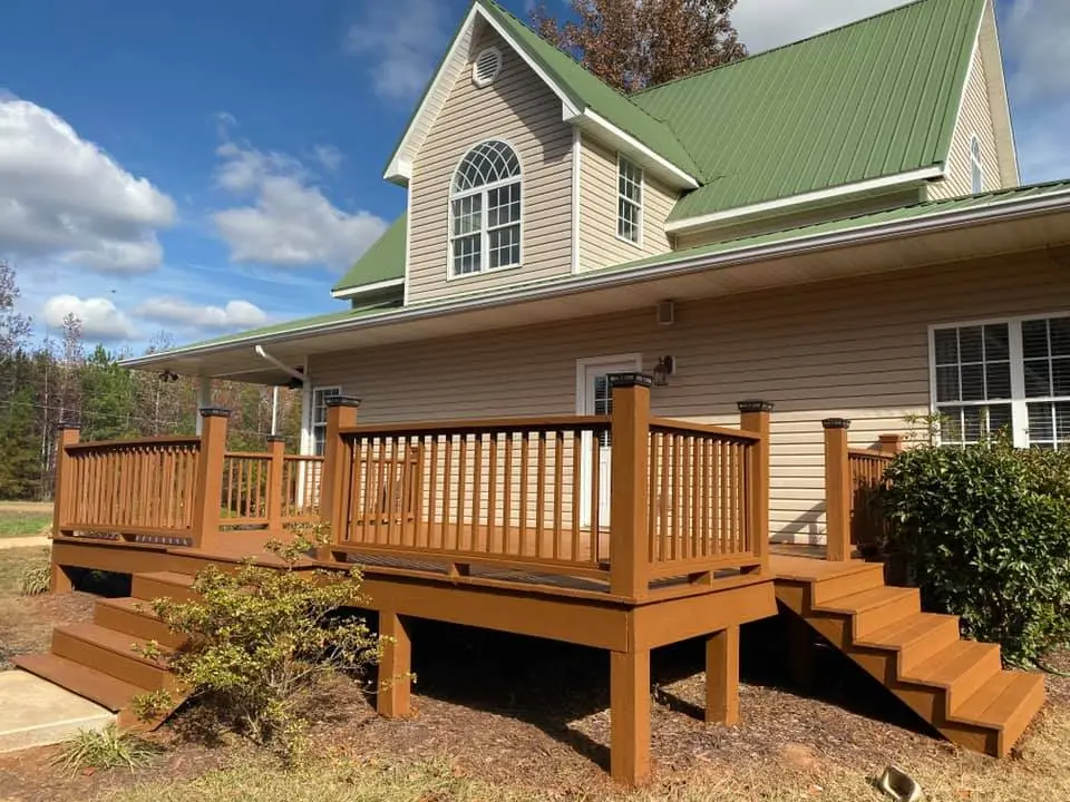 Stained wraparound deck with stairs at a two-story house with a green metal roof