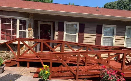 Red-stained deck and ramp with crossed rails at the front of a brick ranch house