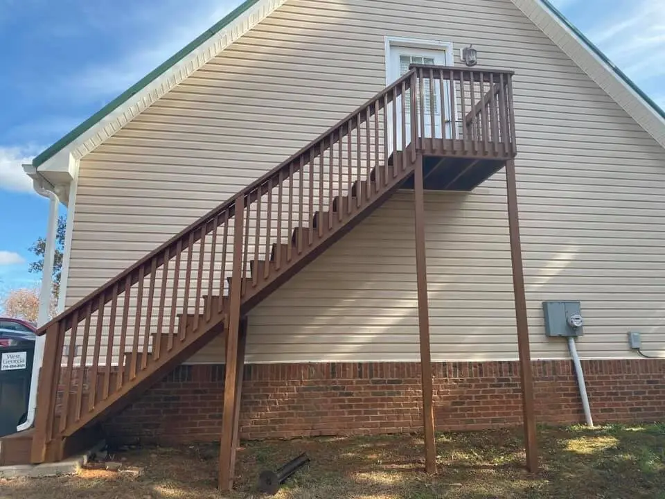 Brown-stained deck staircase climbing two stories at a tan-sided home