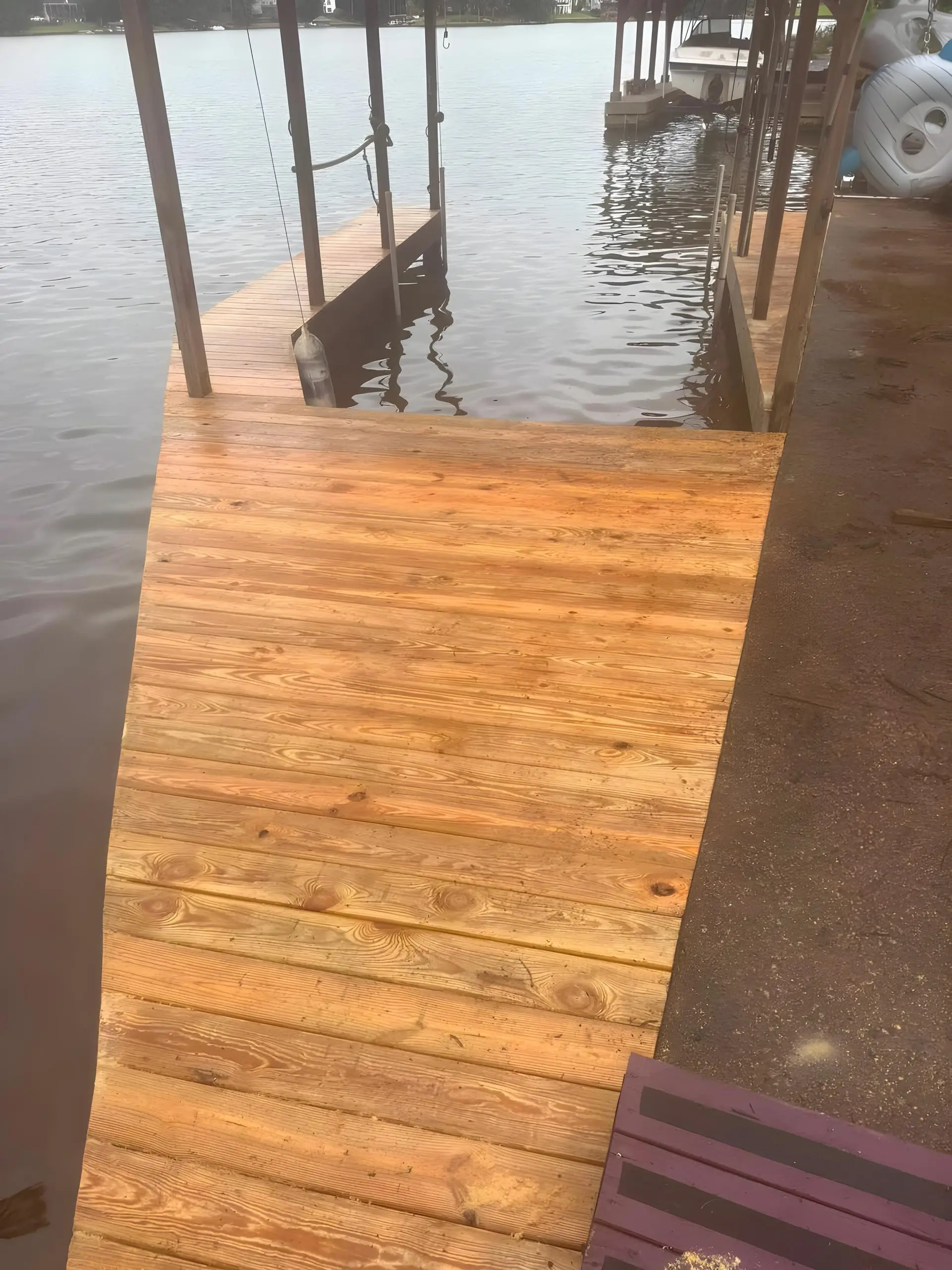 Weathered wood boat dock ramp leading down to the lake with a pontoon boat moored at a covered slip
