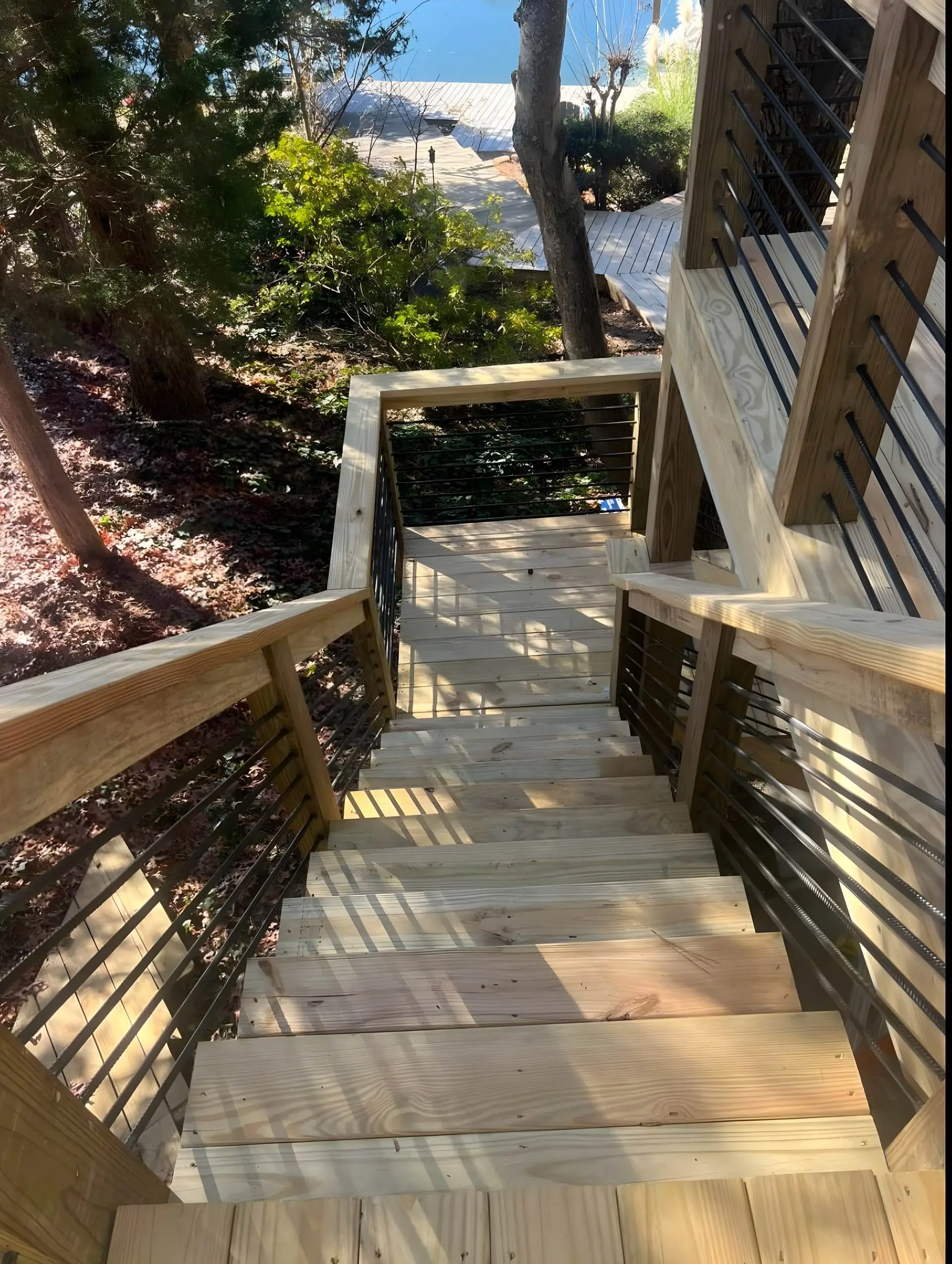 New wood stairs with black cable rail descending toward a covered lake dock