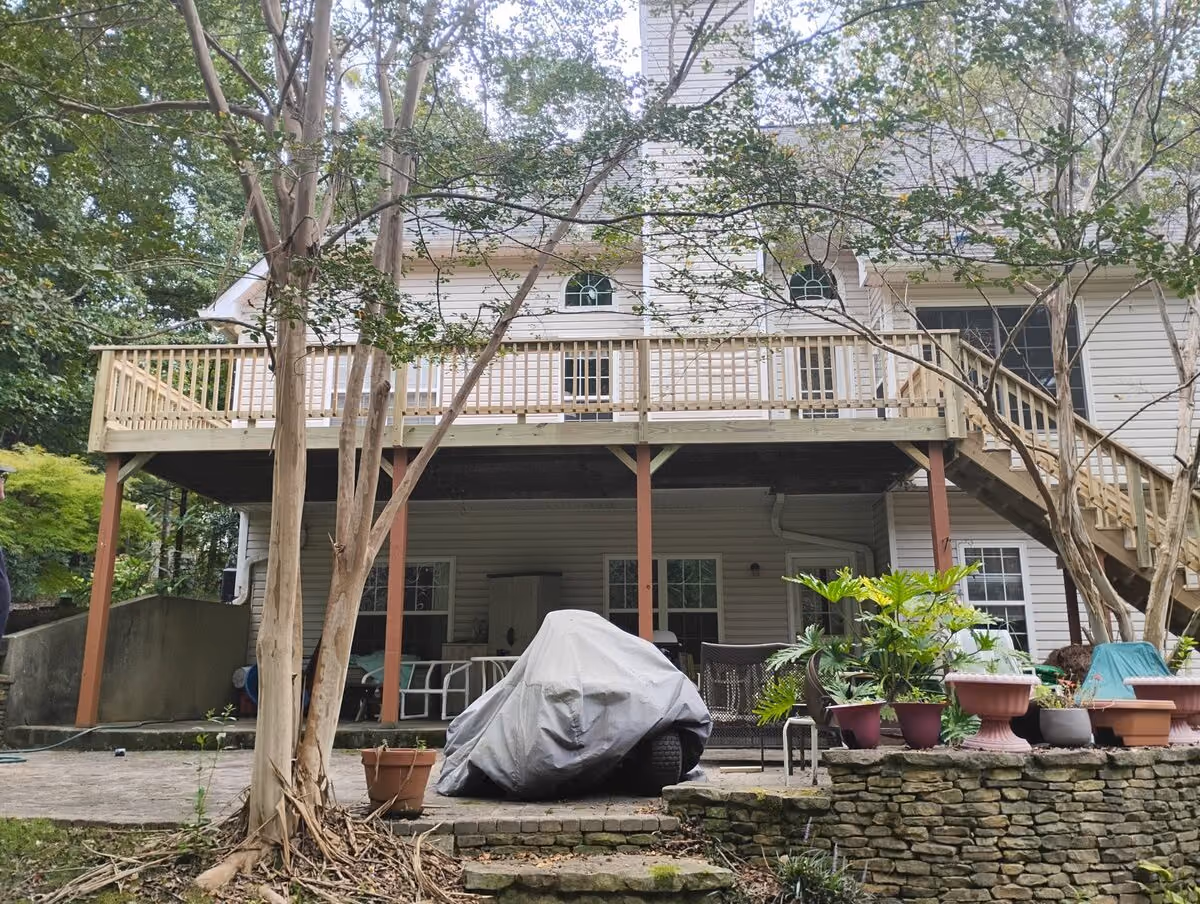 Finished wraparound deck with a stair run and a covered patio beneath it at a two-story home with mature trees