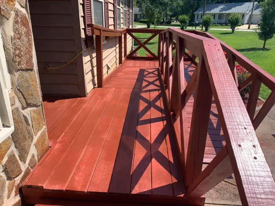 Red-stained wraparound deck ramp with a stone accent wall and cross-brace railing design